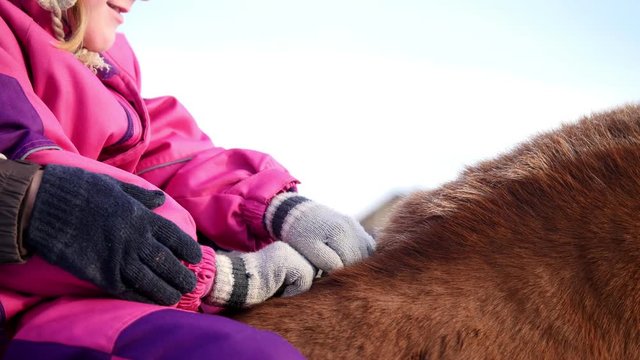 Hippotherapy for kid with cerebral palsy syndrome at winter cold day - contact kids therapy and rehabilitation horse-riding club - young girl and her mother rides on horse, pats horseback, close up