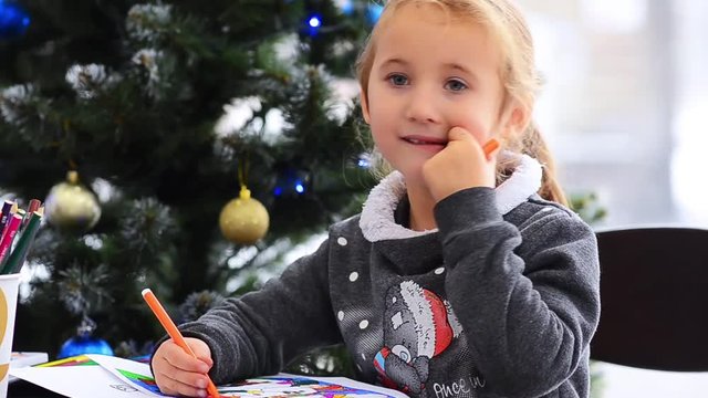 Cute happy little girl playing with crayons. Christmas background. Christmas lights background