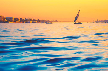 Silhouette of felucca at golden sunset, travel on sail vessel on the Nile river - romantic cruise and adventure in Egypt. Traditional egyptian sailboat on horizon.