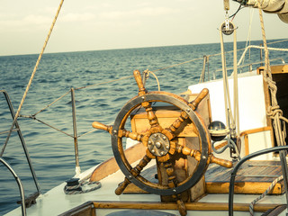 Steering wheel on the old sailboat. Sea voyage of the sailing vessel. Travel at sail boat with a wooden helm in front. Ship wheel on the old yacht - nautical equipment closeup.