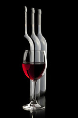 Elegant red wine glass and a wine bottles in black background.