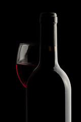 Elegant red wine bottle and wine glass in a black background.