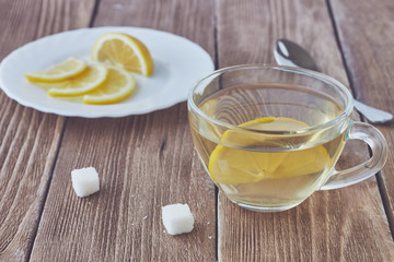 Glass cup of green tea and sliced lemon on wooden background