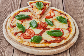Pizza Margherita with tomatoes, mozzarella and basil on a wooden background сlose up.