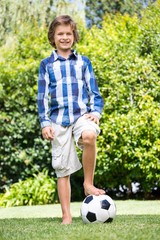 Obraz premium Cute boy smiling and posing with his foot on a soccer ball