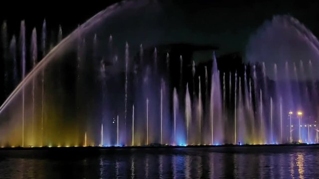 Amazing fantastic colorful fountain with bright illumination on the water pond or river with beautiful reflection at the evening or night. Beauty urban recreational concept.