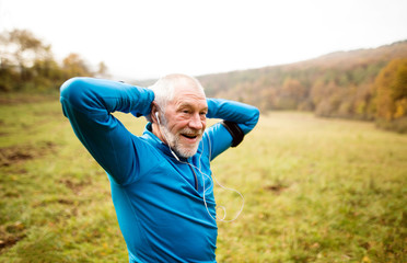 Fototapeta premium Senior runner with armband doing stretching. Autumn nature.