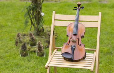Beautiful violin on a wooden chair outdoors. Live music on occasion. Learning to play the violin

