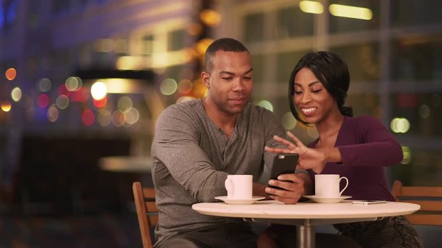 Happy Black couple using smart phone in coffee shop at night