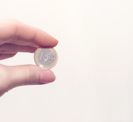 Woman's hand holding a coin one euro on white background. Business concept