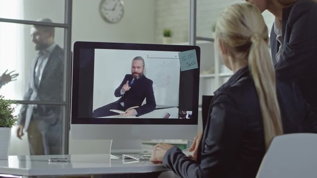 Businesswoman having conversation with CEO via video call on PC while her secretary bringing documents and joining their webinar