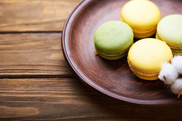 Colorful tasty macaroons at a ceramic plate and cotton flowers on a wooden table. Soft light. Close view.