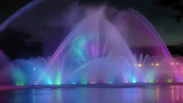 Amazing fantastic colorful fountain with bright illumination on the water pond or river with beautiful reflection at the evening or night. Beauty urban recreational concept.