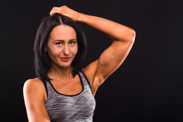 Closeup portrait of beautiful brunette fitness or sports lady smiling for camera while posing isolated on black background in studio.
