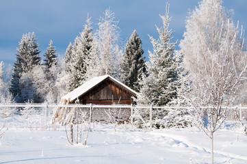 Winter country landscape with wooden house behind a fence in the forest