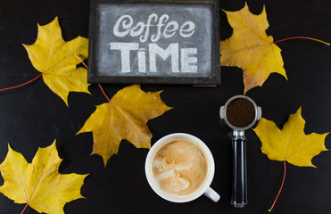 cup of cappuccino coffee while autumn leaves chalk on a blackboard