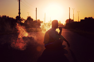 The man smokes on the road at sunset