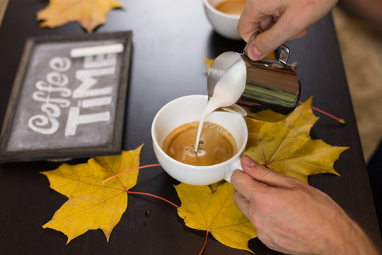 cup of cappuccino coffee while autumn leaves chalk on a blackboard