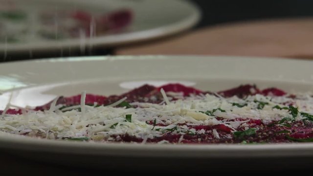 Serving carpaccio meat dish with parmesan cheese slow motion сlose up HD video. Cheese falling on raw beef slices. Cooking on restaurant kitchen 