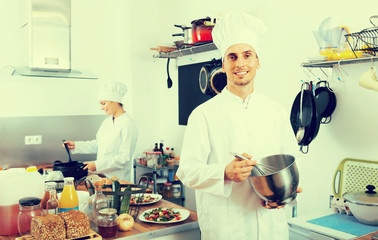 Smiling young man chef cooking food at kitchen