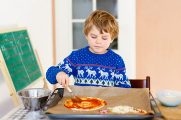 Cute little kid boy making italian pizza with fresh vegetables