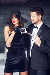 Sexy dominatrix woman holding on handcuffs young macho lover in
