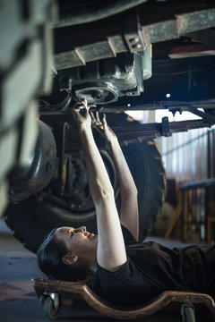 Woman lying on creeper under car in workshop