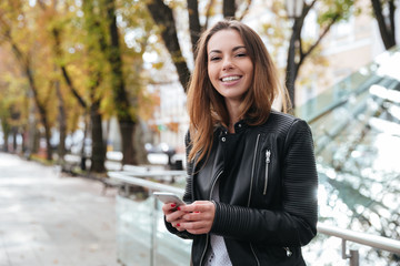 Cheerful woman standing and using smartphone in the city