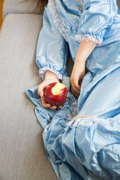 Little girl dressed up as a princess holding bitten red apple, partial view