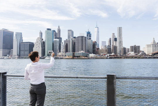 USA, Brooklyn, businesswoman taking picture of Manhattan skyline