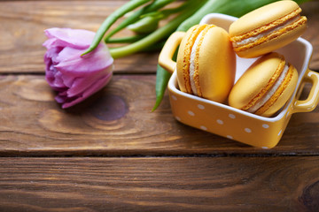 orange macaroons in yellow vase with purple tulip on a wooden table. Soft light. Close view.