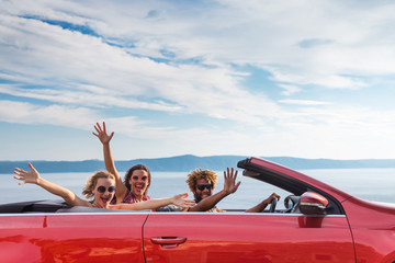 Group of happy young people waving from the red convertible.