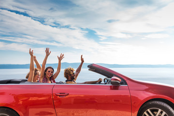 Group of happy young people waving from the red convertible. - obrazy, fototapety, plakaty