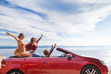 Group of happy young people waving from the red convertible.