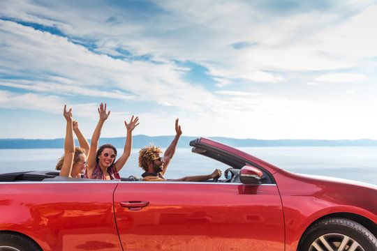 Group of happy young people waving from the red convertible.