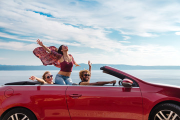 Group of happy young people waving from the red convertible. - 128746852