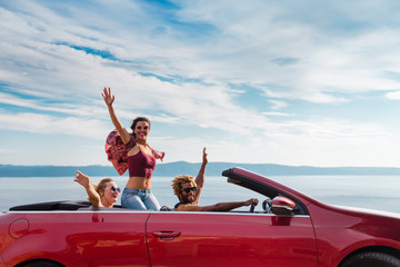 Group of happy young people waving from the red convertible.