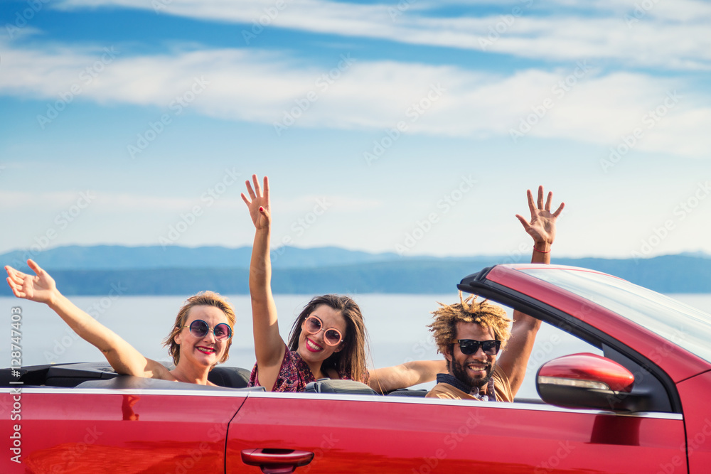 Wall mural group of happy young people waving from the red convertible.