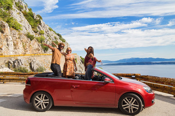 Group of happy young people waving from the red convertible.