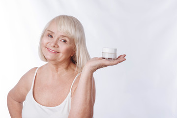Optimistic aged woman holding a moisture cream bottle
