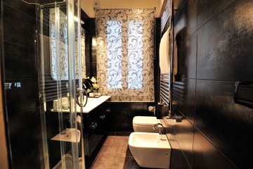 Italian bathroom with black wall / tiles and white forniture / services. A warm light illuminates the room