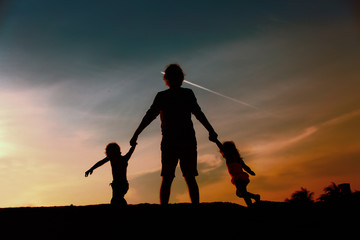 father with son and daughter silhouettes play at sunset
