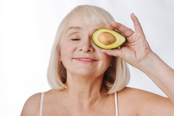 Charming pleasant woman holding an avocado half near the eye