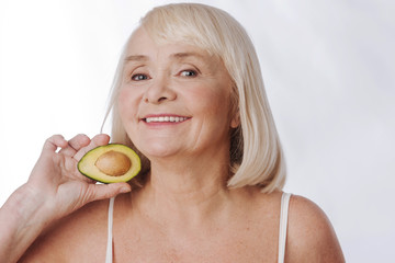 Joyful aged woman holding half of an avocado