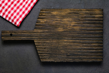 Wooden cutting board and classic red checkered textile on dark background. Top view, copy space for text