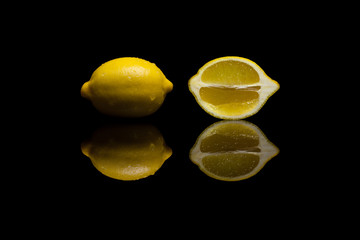 One whole and one cut yellow lemon on black background