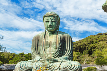 The Great Buddha in Kamakura Japan which is surrounded by green leaves.