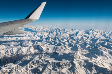 Aerial view of the Italian Swiss Alps in winter, with generic aeroplane wing. Snowcapped mountain...