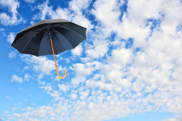Black umbrella flies in sky against of pure white clouds.Mary Poppyns umbrella.Wind of change concept.