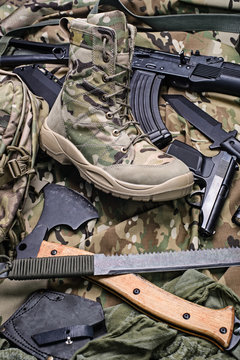 One army boot and different weapon.Selective focus/Military boot, an ax, pistol and rifle top view.Selective focus